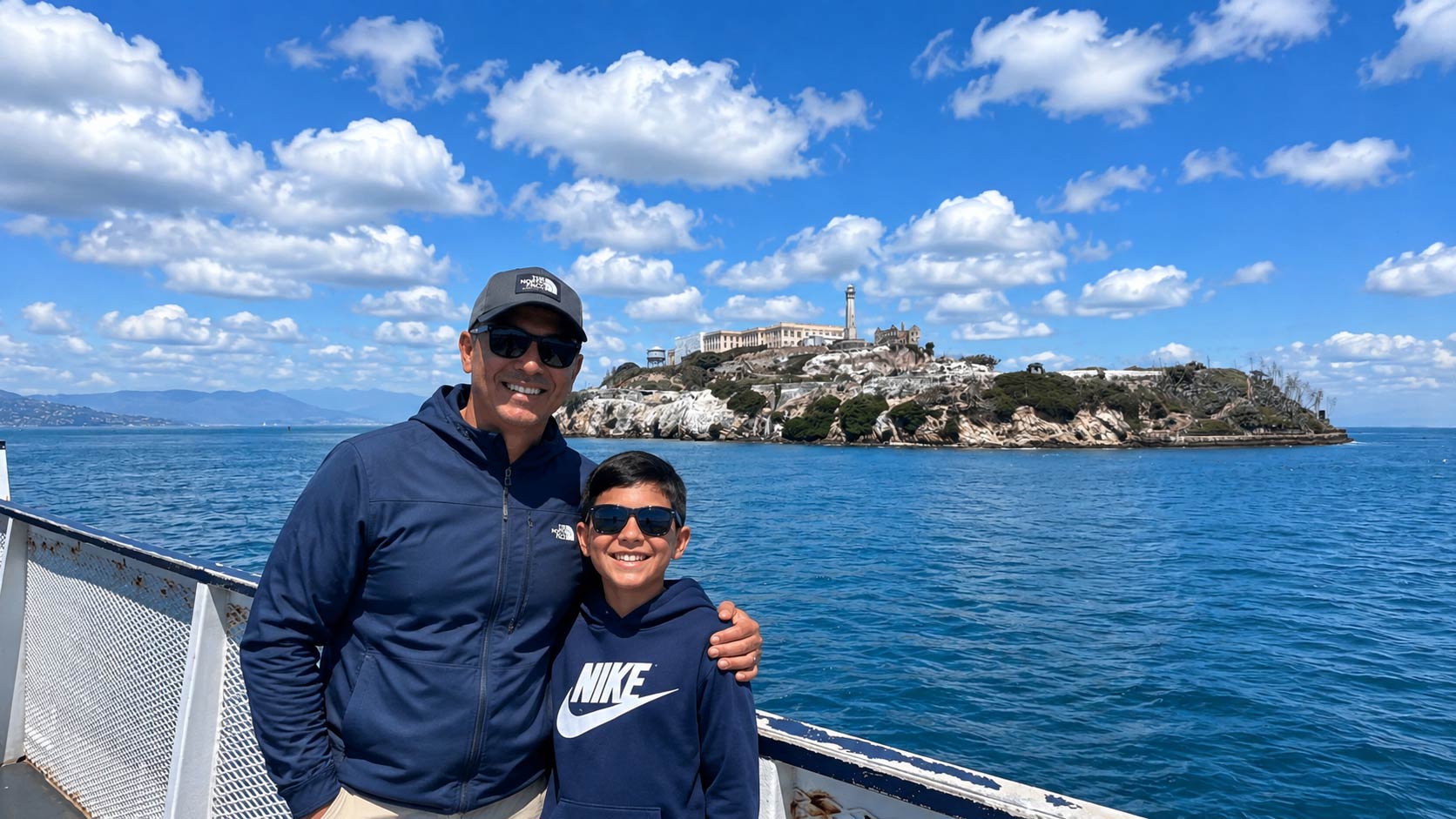 A father and sun take a photo in front of Alcatraz Island.